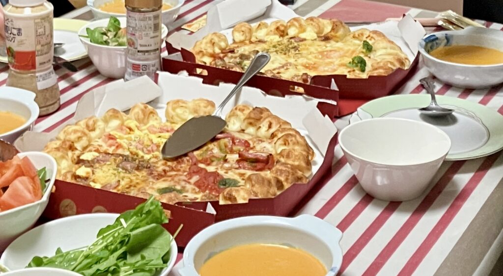 出前のピザとサラダ、エビのビスクを並べた食卓
